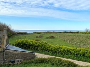 A stone house with a metal roof, surrounded by green fields and a wooden fence. - New house 3 rooms, near beach in Locmaria, sleeps 6-8 (Groix)
