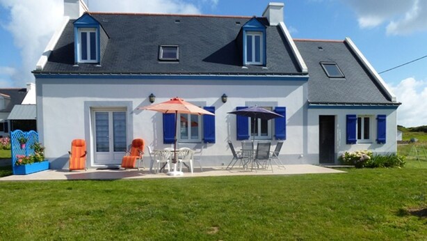 Une maison à deux étages dotée d’un patio aménagé avec des meubles d’extérieur et des parasols.