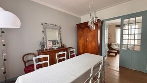 Ein Esszimmer mit einem großen Tisch, Stühlen, einer Holzkommode, einem Spiegel und einer Chandelier.