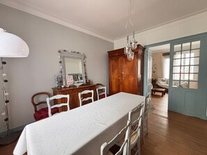 A dining room with a large table, chairs, a wooden cabinet, a mirror, and a chandelier. - 3-bedroom house, city center, beach access, WIFI included (Les Sables-d'Olonne)
