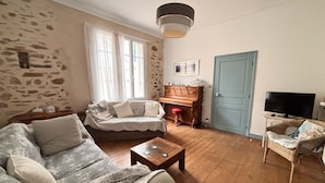 Ein gemütliches Wohnzimmer mit einer Couch, einem Holztisch, einem Klavier und einem Fernseher.