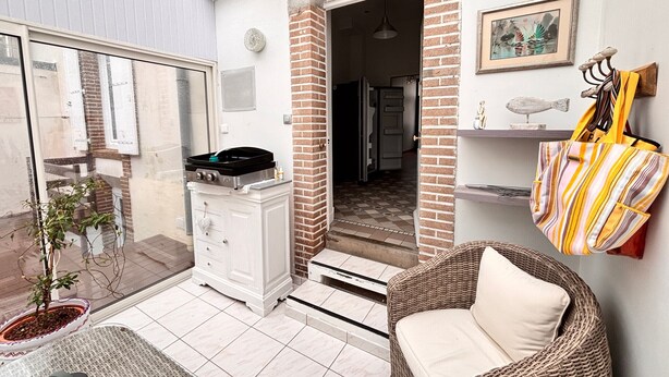Eine Terrassenfläche mit einem Korbstuhl, einem kleinen Tisch, einer Kübelpflanze und einem weißen Schrank mit einem Gasherd.