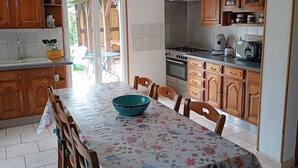 A kitchen with wooden cabinets, a dining table with chairs, a stove, and a microwave. - Spacious Lodge in Nargis with Private Parking, Near Paris (Nargis)