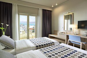 Una habitación de hotel con dos camas, un escritorio, una silla, un televisor y un ventanal con vistas a una ciudad y montañas.