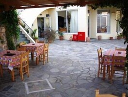Un patio al aire libre con piso de piedra, mesas de madera con manteles a cuadros y plantas en macetas.