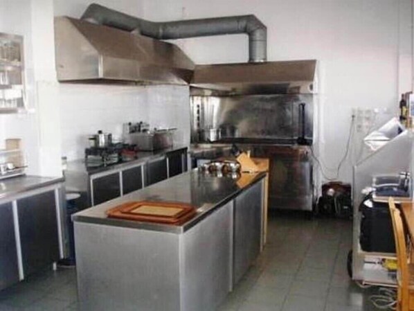 Cocina comercial con electrodomésticos de acero inoxidable, una isla central y un sistema de ventilación.