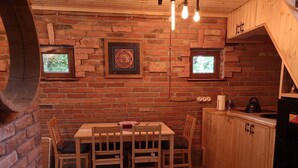 A rustic kitchen with a brick wall, wooden cabinets, a dining table with chairs, and a small window.