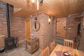 Ein gemütliches Zimmer mit Kamin aus Backsteinen, Holzbalkendecke und einem Esstisch mit Stühlen.