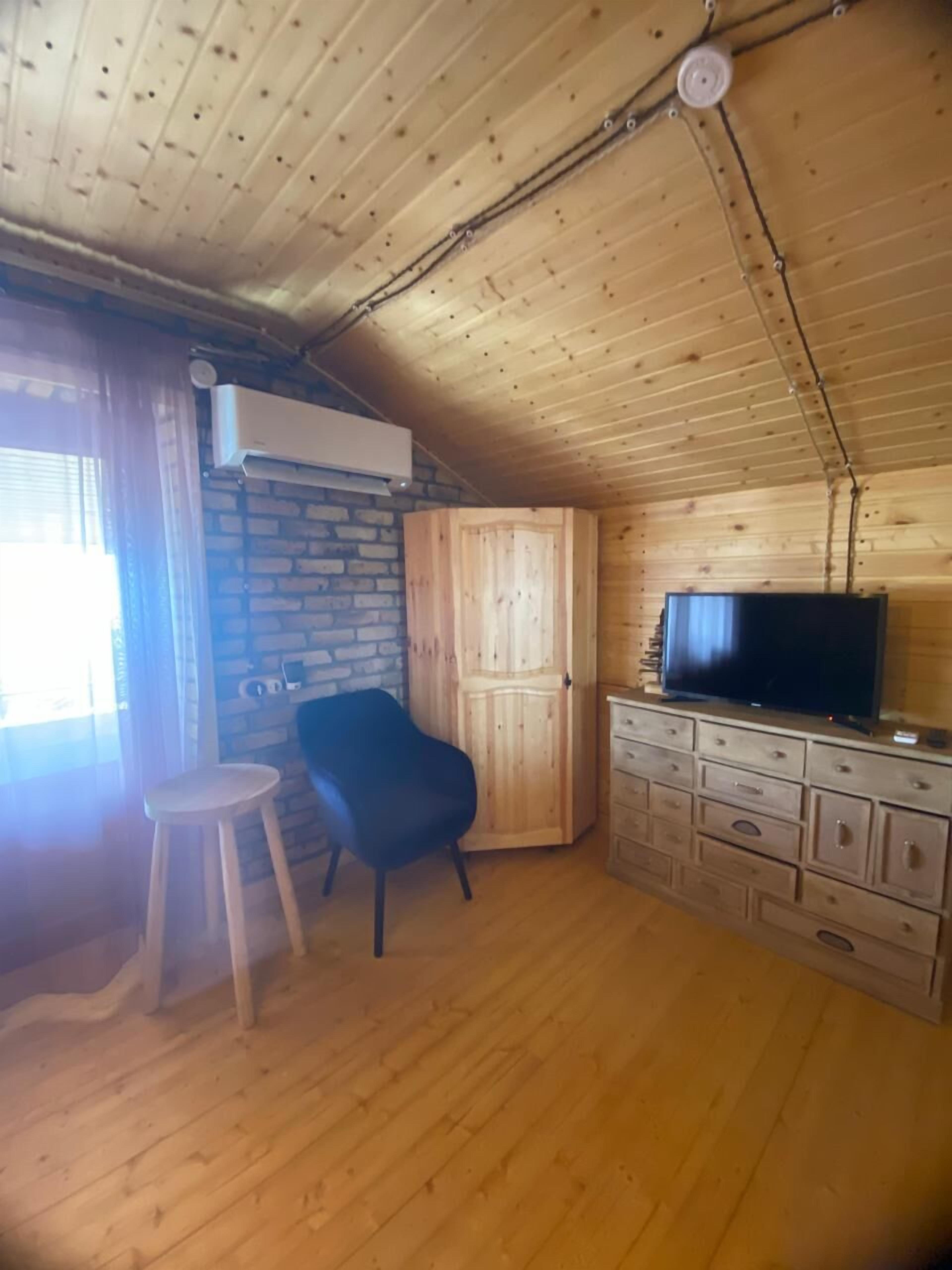 Een houten interieur met een televisie op een dressoir, een stoel en een klein krukje.
