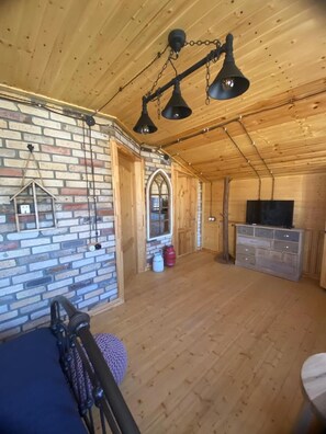 Ein Holzblockhaus-Interieur mit Backsteinwand, Schlafkoje, Fernseher und Kamin.