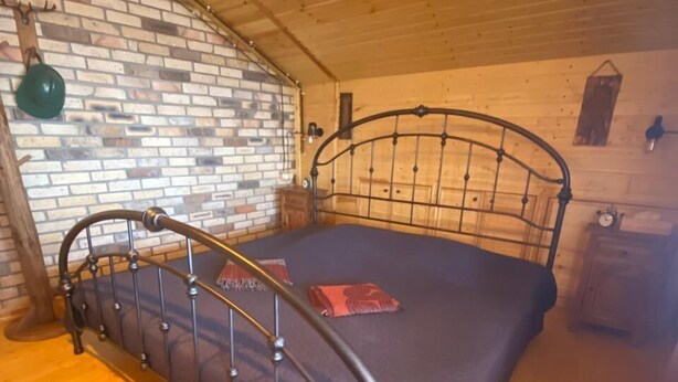 A wooden-paneled room with a metal-framed bed, a brick wall, and a wooden floor.