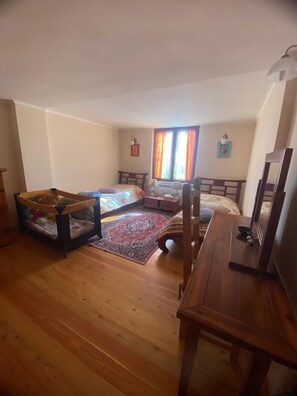 Ein Zimmer mit zwei Betten, Holzboden, Schreibtisch und einem Fenster mit Vorhängen.