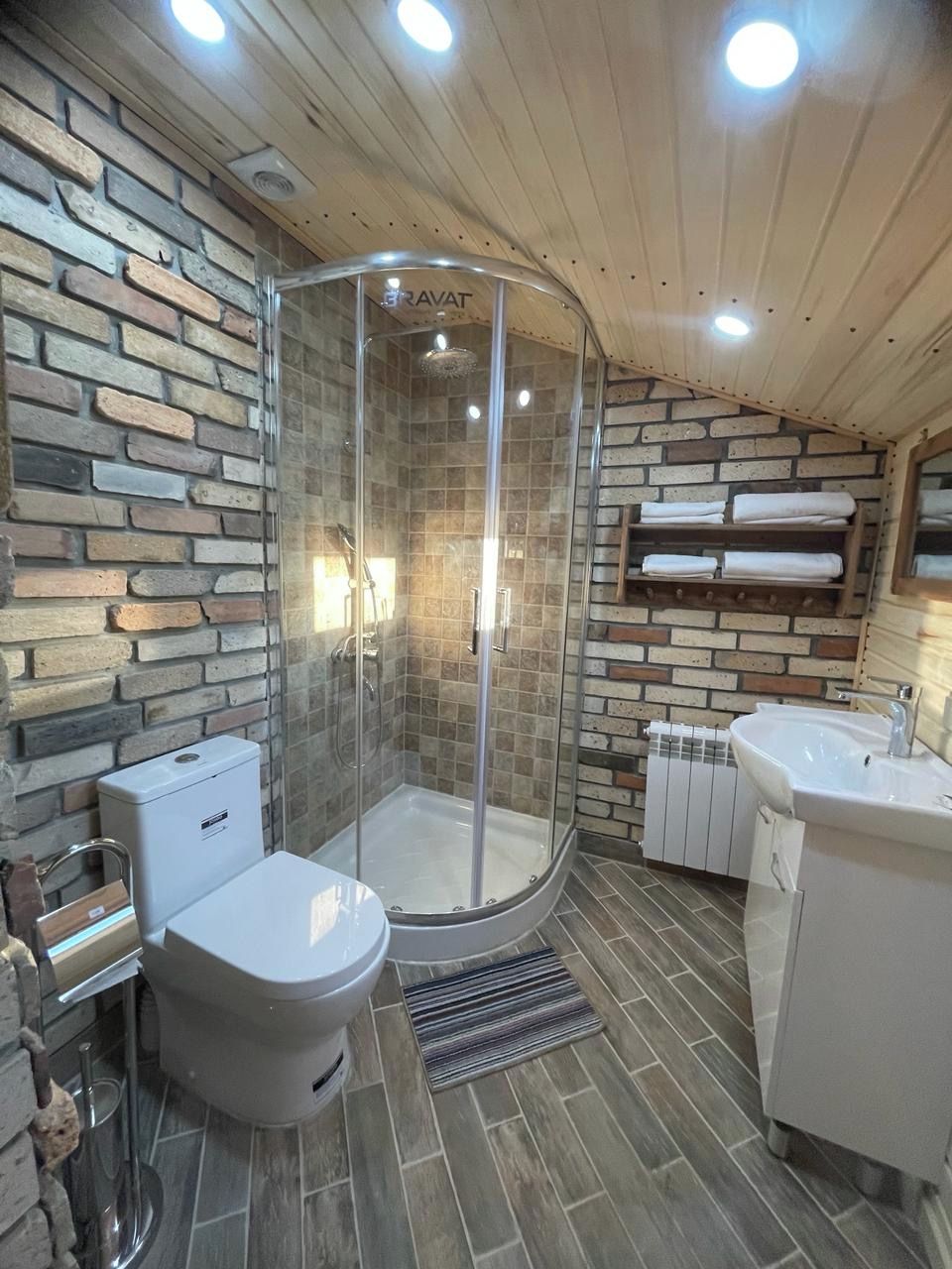 Un baño con ducha envuelta en vidrio, inodoro, lavabo y perchero para toallas.
