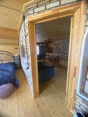 Tunnelmallinen hirsihuvilan sisustus, jossa on parvelle sijoitettu sänky, sininen sohva ja ruokailutila, jonka taustalla on tiiliseinä.