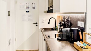 A compact kitchen with a sink, a coffee maker, and a kettle. There are papers on the wall and a bag hanging on the wall. - Luna Apartment Passau - Balcony - Kitchen - Self Checkin - Parking lot (Passau)