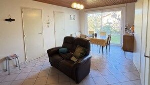 Un salon chaleureux avec un canapé en cuir, une table à manger et des chaises, ainsi qu’une grande fenêtre offrant une vue sur l’extérieur.