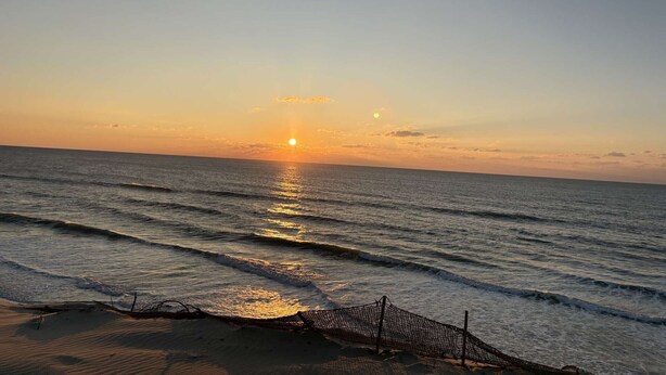 Une scène de plage au coucher du soleil sur l’océan, avec des vagues qui viennent doucement lécher le rivage et un filet de pêche étendu sur le sable.