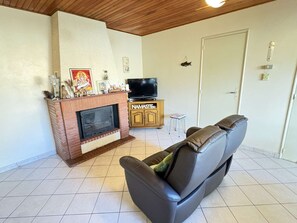 Ein Wohnzimmer mit Kamin, Fernseher, Sofa und einem Schrank mit der Aufschrift 'NAMASTE'.