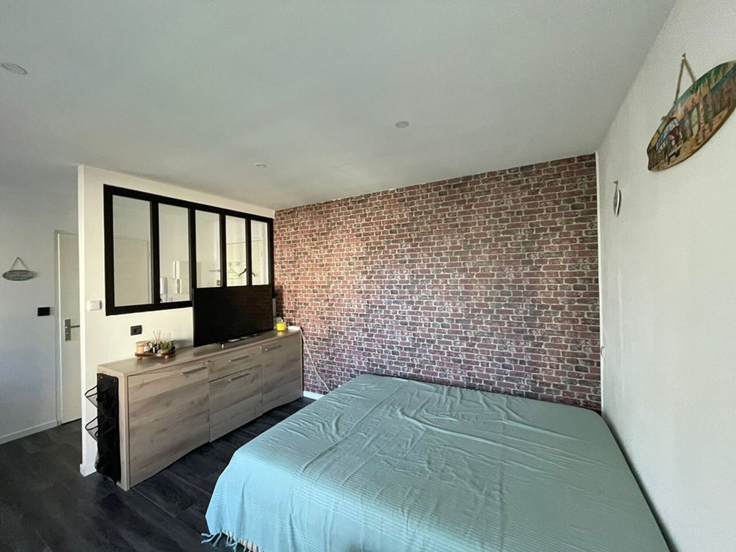 Een slaapkamer met een bakstenen muur, een bed, een dressoir en een aan de muur bevestigde televisie.