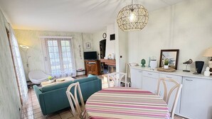 Uma sala de estar aconchegante com sofá, mesa de jantar com cadeiras, televisão e área de cozinha com armários e bancada.