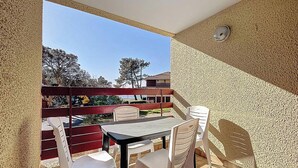 Een balkon met een tafel en stoelen, een rode leuning, en uitzicht op bomen en gebouwen.