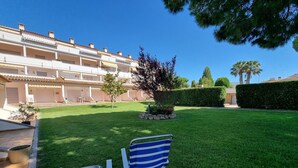 A courtyard with two striped chairs, a small tree, and a building with balconies. - Apartment 400m from the beach with communal pool (L'Escala)