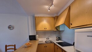 A compact kitchen with wooden cabinets, a microwave, a kettle, and a built-in stove. - Apartment 400m from the beach with communal pool (L'Escala)