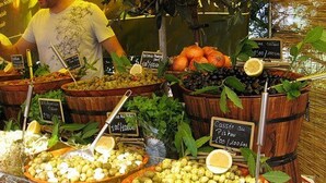 Ein Marktstand mit verschiedenen Früchten und Gemüsen, präsentiert in Holzfässern und Körben, mit Preisschildern.