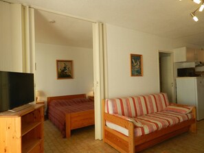 A small, cozy room with a bed, a sofa, a television, and a kitchen area. - 2-Room Apartment, Sleeps 4, Parking, WIFI - Le Lavandou (Le Lavandou)