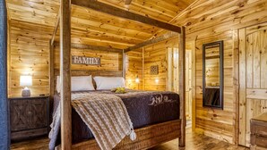 A wooden four-poster bed in a cabin-style room with a 'FAMILY' sign above it, a small nightstand with a lamp, and a mirror on the wall. - Royal Bliss - Mountain Views Theater Hot Tub (Sevierville)