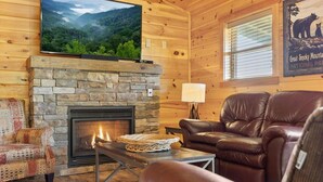 A cozy cabin interior with a stone fireplace, leather seating, a mounted TV, and a framed poster of Great Smoky Mountains National Park. - Royal Bliss - Mountain Views Theater Hot Tub (Sevierville)
