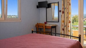 Un dormitorio con cama, escritorio, silla, televisor y ventana con cortinas.