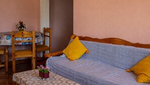 Una habitación acogedora con una silla y una mesa de madera, un sofá azul con cojines amarillos y una pequeña planta en maceta.