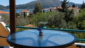 Una mesa redonda de cristal con una planta en maceta en un balcón que da a un pueblo costero con montañas al fondo.