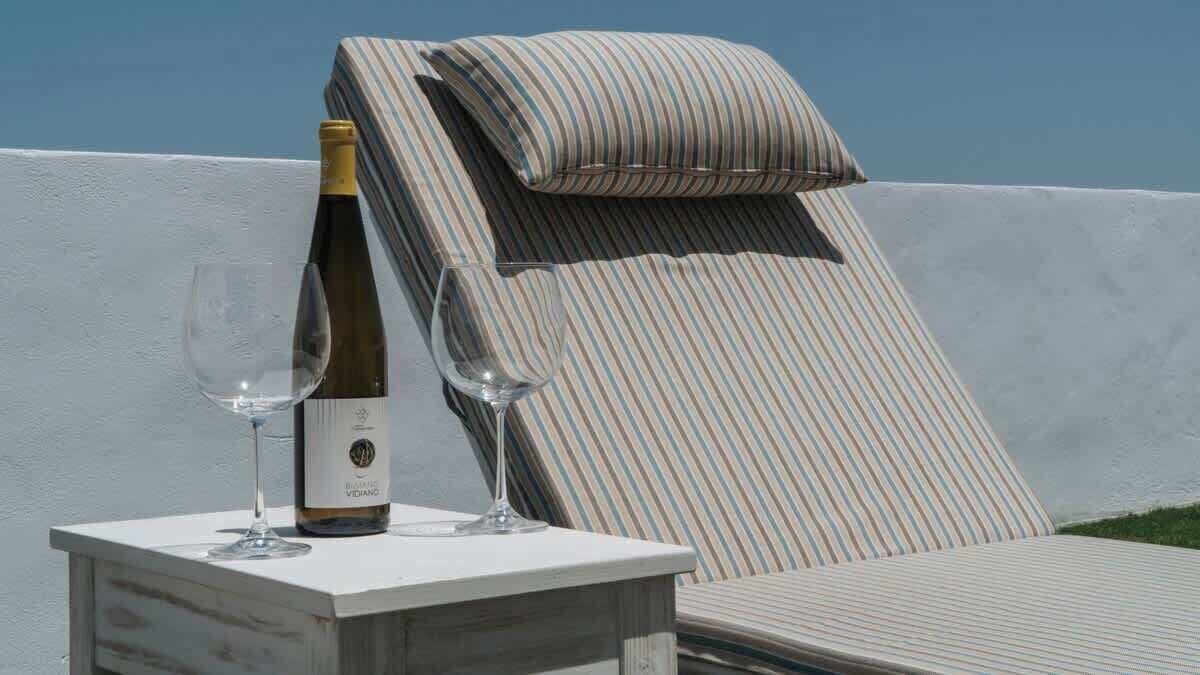 A lounge chair with striped cushions and a bottle of wine on a white table.