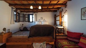 Un dormitorio acogedor con una cama de madera, un pequeño sofá, una mesa de madera y una ventana con cortinas.