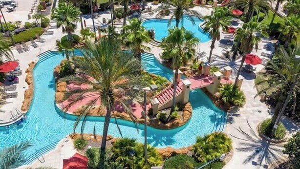Ein Poolbereich eines Resorts mit mehreren Pools, Palmen und Liegestühlen.