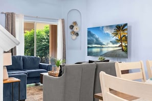 Un salon avec un canapé, une table à manger et un téléviseur diffusant une scène de plage.