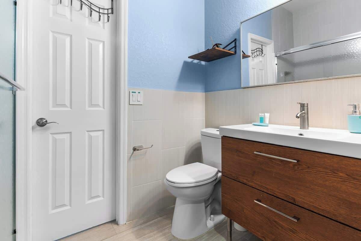 Een badkamer met een wit toilet, een houten wastafelmeubel en een spiegel boven de wastafel.