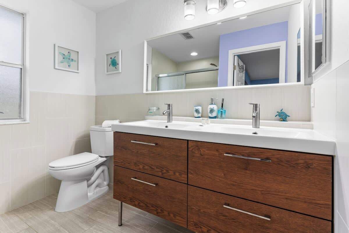 Ein Badezimmer mit einer weißen Toilette, einem Holzausziehtisch mit Schubladen, einem großen Spiegel und zwei gerahmten Bildern an der Wand.