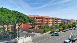 Un immeuble à plusieurs étages avec une façade rouge, un parking rempli de voitures et un ciel bleu clair.