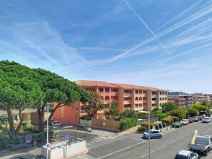 A multi-story building with a red facade, a parking lot with cars, and a clear blue sky. - T2 with Loggia in La Favière - 5 Guests + Parking (Bormes-les-Mimosas)