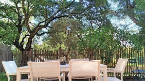 Une terrasse avec une table et des chaises, entourée d’arbres et d’une clôture en bois.