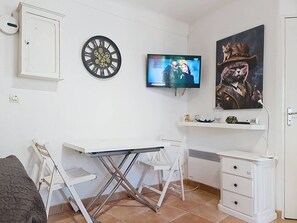 A compact room with a white desk, a television, a clock, and a painting of a cat in a hat. - T2 Cabin 33m², Terrace, Parking, 6 Pers (Bormes-les-Mimosas)