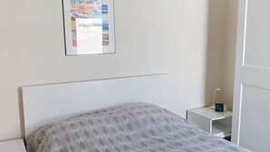 Ett sovrum med en säng, ett sängbord, en liten avlastningsyta, en tavla som hänger på väggen och en dörr.