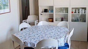 En matplats med ett bord dukat för fyra personer, omgiven av vita stolar. Där finns också ett vitt skåp med glasdörrar där tallrikar och glas står framme.