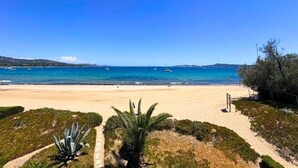 Une plage avec un ciel dégagé, un rivage sablonneux et quelques bateaux sur l’eau.