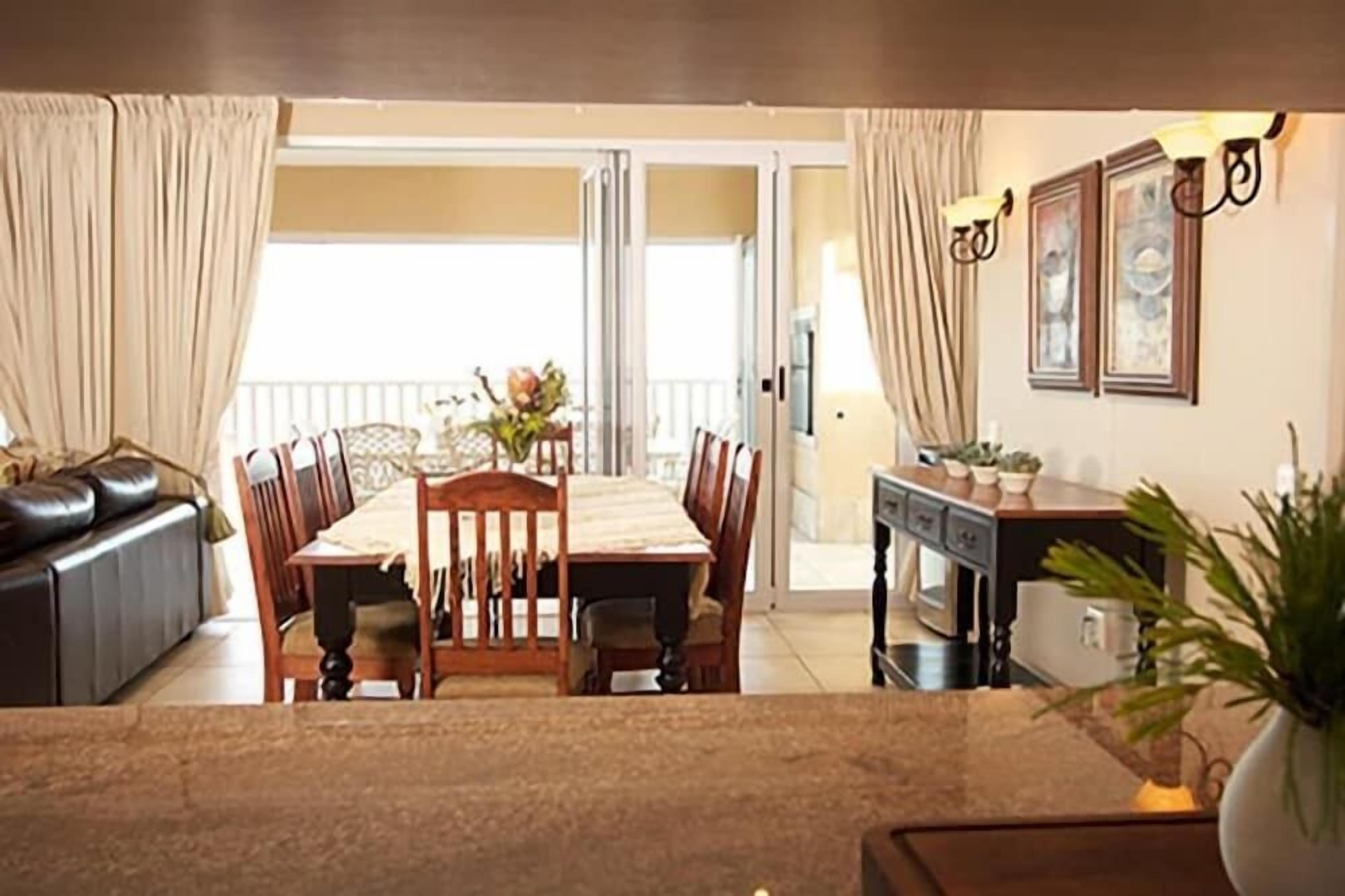A dining area with a table and chairs, a sofa, a small cabinet, and a plant.