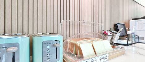 Dos tostadoras azul claro sobre una encimera de mármol, con una caja de pan de plástico transparente que contiene pan blanco.