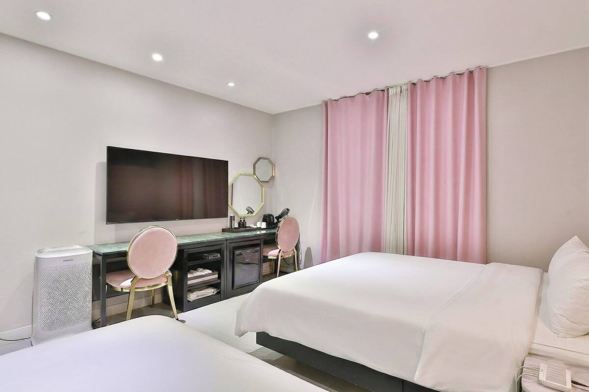 A hotel room with two beds, a desk, a chair, a television, and a mirror.